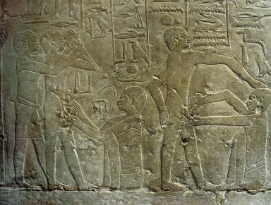 Relief with hieroglyphs above standing figures while others sit and perform circumcisions. 