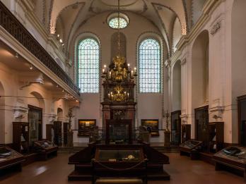 Photograph of room interior with Torah ark, chandelier, and tall arched doorways.
