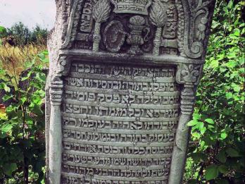 Photograph of tombstone with Hebrew text, engraved columns, and decorative objects on top.