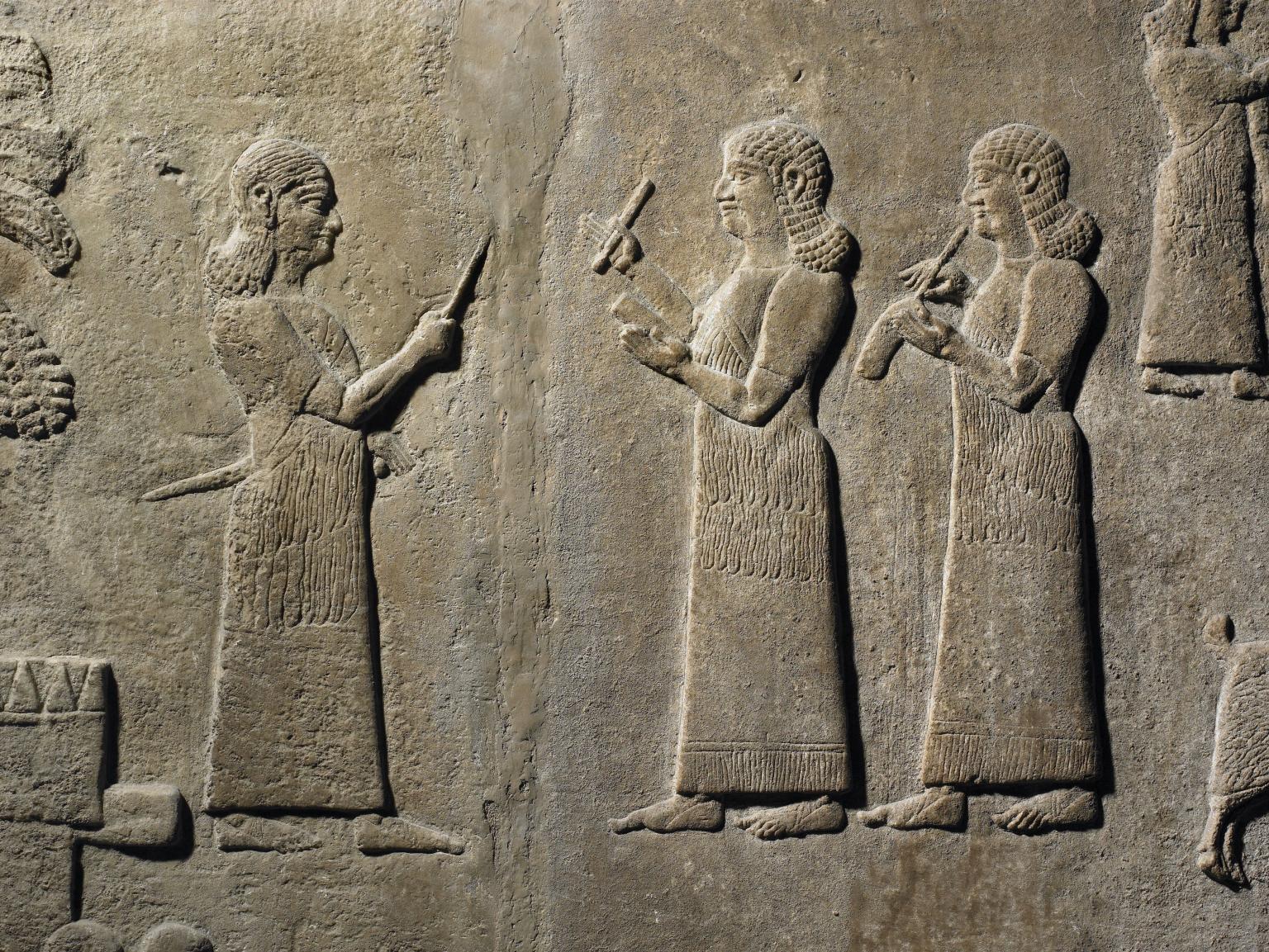 Relief of two standing figures in profile, wearing long tunics and curly hair, writing and another figure standing opposite them.