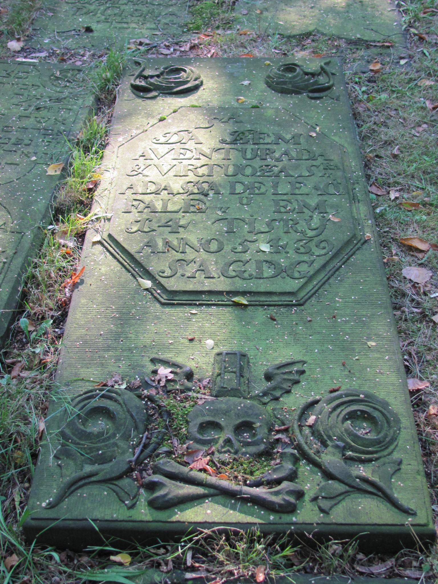 Gravestone on ground with inscription and engraving of skull and bones.