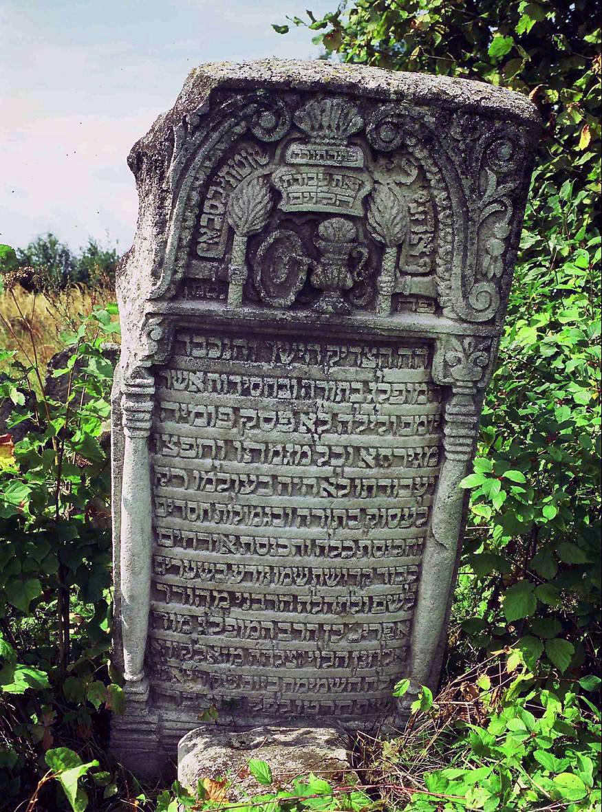 Photograph of tombstone with Hebrew text, engraved columns, and decorative objects on top.