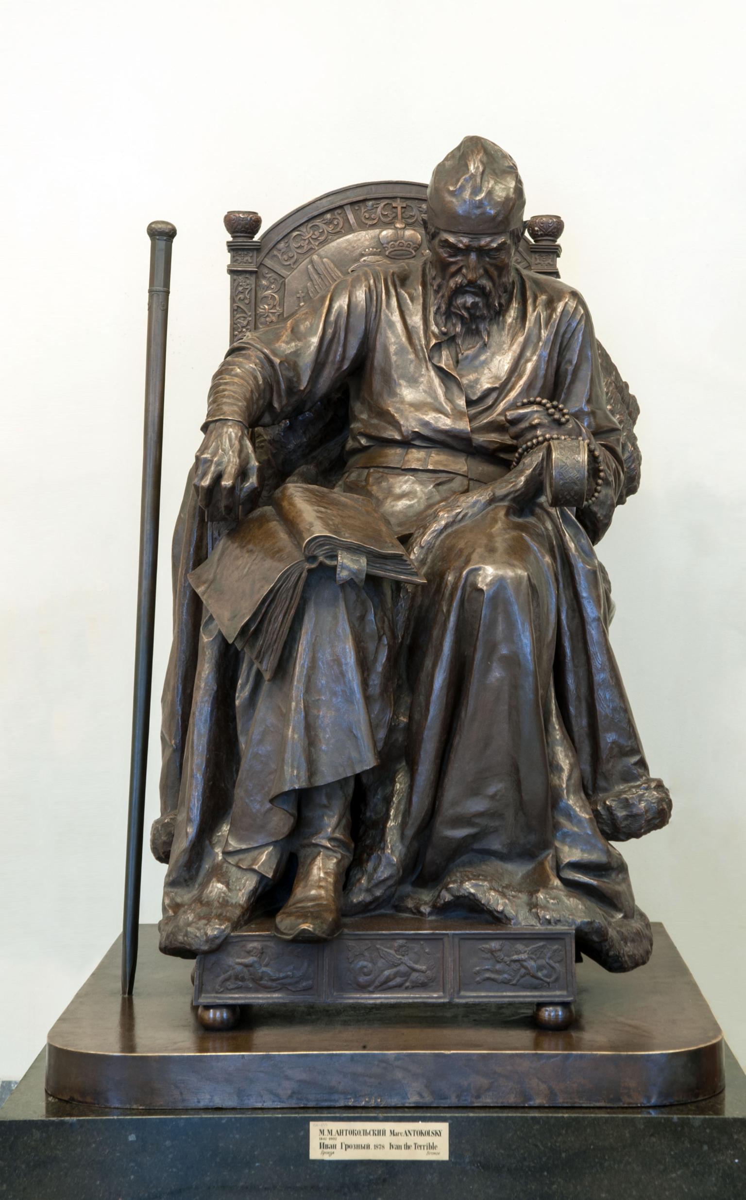 A sculpture of man with book and beads seated on throne.