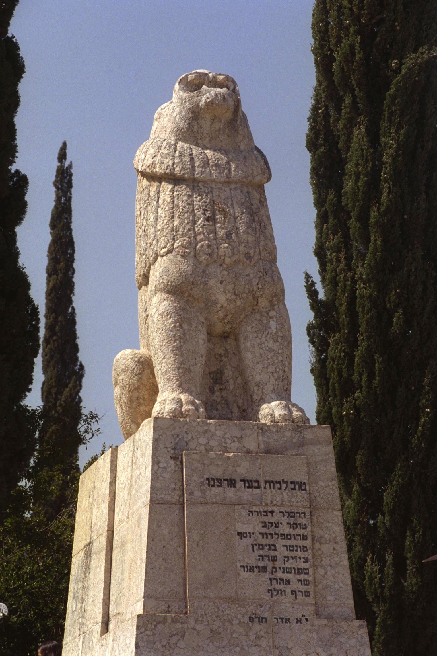 Statue of a lion roaring toward the sky on pedestal with Hebrew writing.