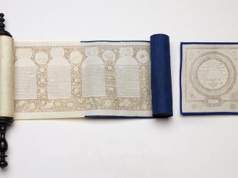 Partially unraveled scroll with Hebrew text in rounded columns and decorative border and individual page next to it with Hebrew text and circular border. 