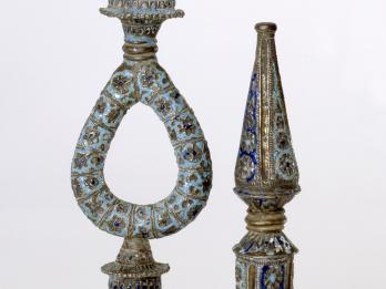 Two finials, one with a loop in the middle, decorated with flowers and lines.