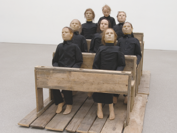 Art installation of eight figures sitting on pews. 
