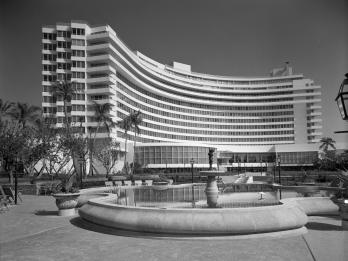 Photograph of curved exterior of a hotel with pool and fountain in the middle.