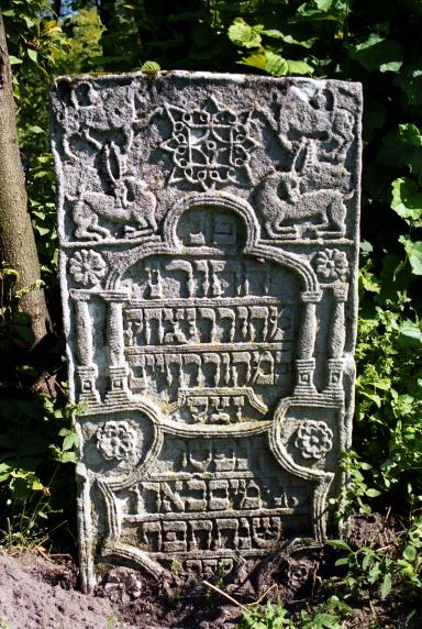 Tombstone with Hebrew inscription in geometric shape with columns and animals surrounding.