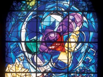 Stained glass window featuring large circle in center and a wolf in bottom right corner devouring prey.