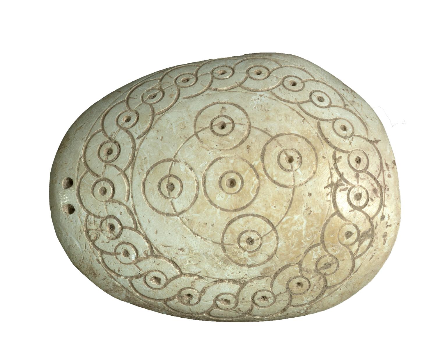 Oval-shaped seashell incised with concentric circles, spirals, and dots in center of circles. 