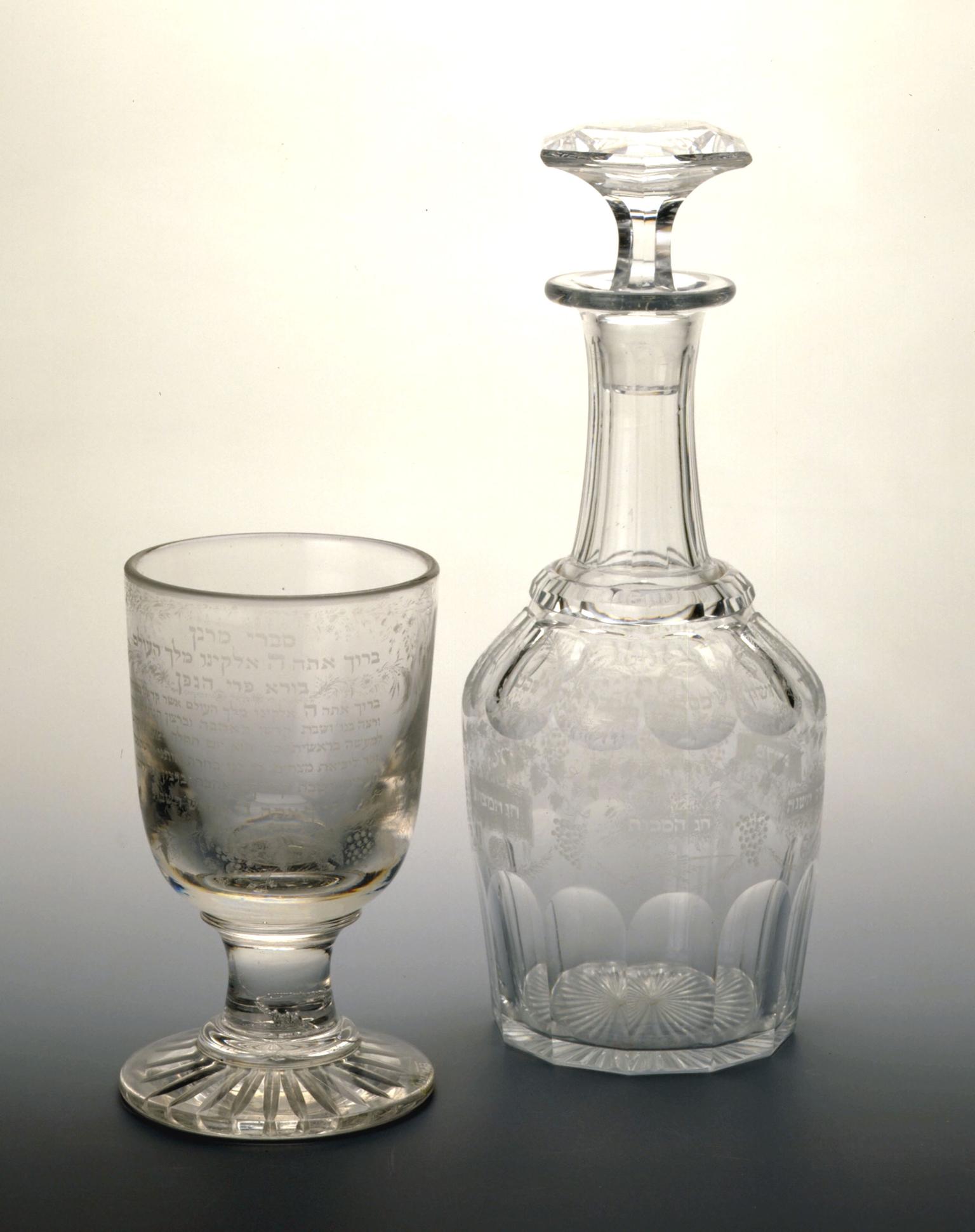 Glass cup and carafe with designs and Hebrew text etched on the outside.
