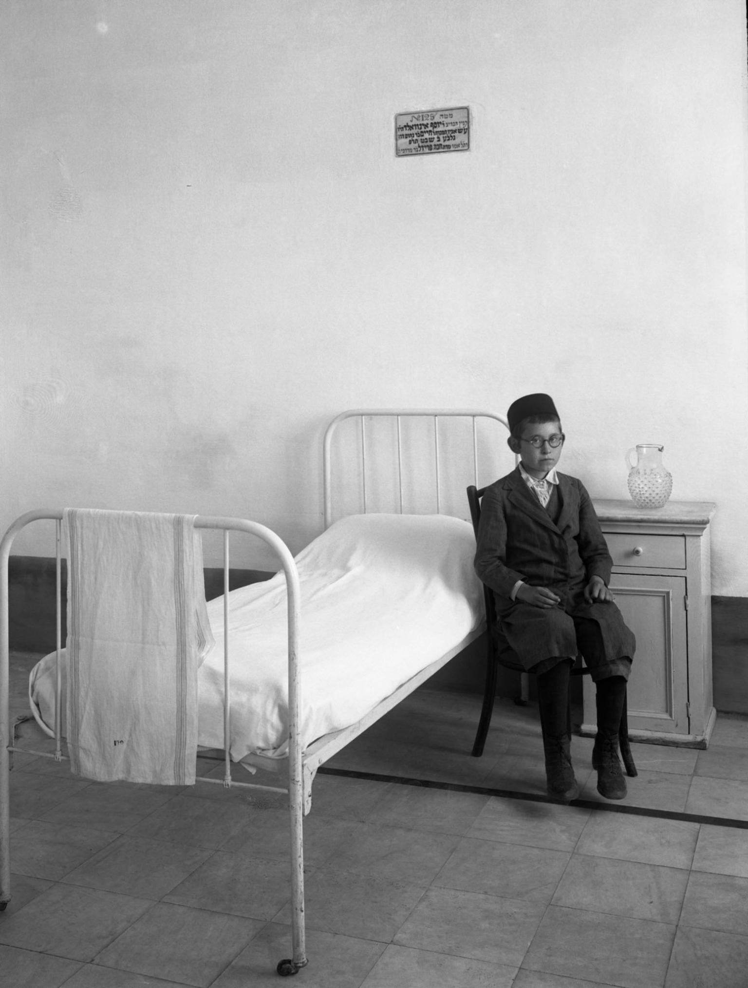 Photography of young boy sitting next to bed and nightstand.