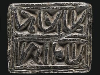 Photo of a rectangular black stone block inscribed with two outlined words of reversed Hebrew writing.