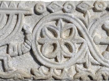 Stone relief featuring a candelabrum, horn, and plant bundle, floral patterns, and floral and geometric borders.