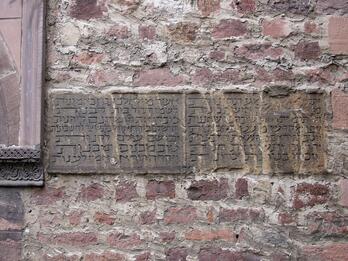 Photo of a weathered stone plaque with Hebrew inscriptions set into a rough brick wall.