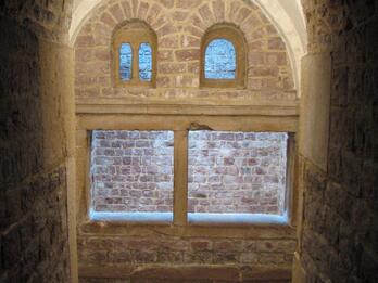 Photo of a stone stairway descending to an arched alcove with two arched windows above a larger rectangular window.