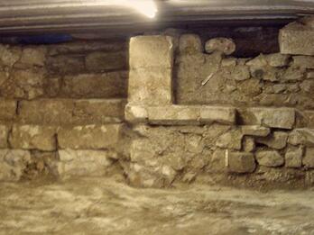 Photo of the bottom part of a stone and brick room with rough, uneven walls and partial columns.