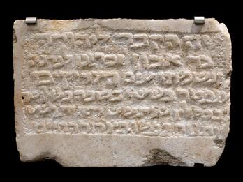 Rectangular white stone tablet with six lines of Hebrew relief text.