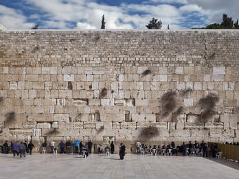 Photograph of large stone wall with many people in front praying.