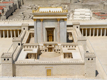 A detailed model of a temple, featuring stone walls, columns, golden accents, and surrounding courtyards, with other structures visible in the background.