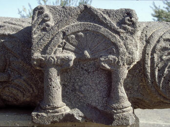 Weathered stone carving featuring two short columns supporting an arch with a fan-like design inside.