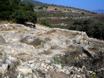Ruins of buildings in rectangular plans set among greenery atop a mountain.
