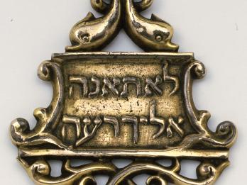 Bronze amulet with decorative border and Hebrew inscription.