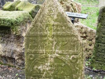 Tombstone in graveyard with triangular top, Hebrew inscription, and Star of David. 