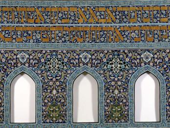 Faience-tile mosaic of floral designs throughout, two lines of Hebrew text at the top, and three niches at bottom.  