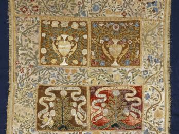 Cloth embroidered with floral border, and four central panels, the top two with pitchers, vines, and flowers, and the bottom two with trees and ribbons with Hebrew text. 