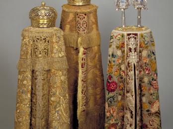 Three cylindrical embroidered cloth covers, two with crowns on top and one with two finials on top. 