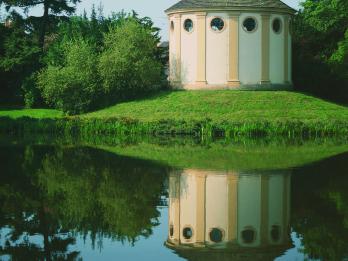 Photograph of round building in a park, reflected in pond.