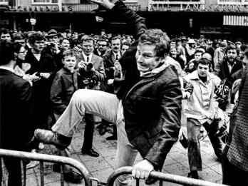 Photograph of a man jumping barricade in front of crowd of people.