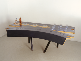 Sculpture of a cracked table with set of drinking glasses and glass ashtrays on it. 