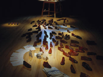 Installation featuring various objects, shoes, and papers on floor. 
