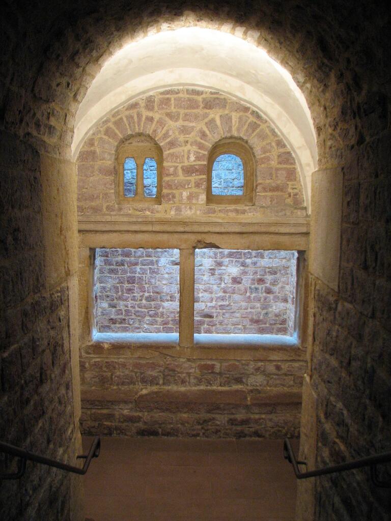 Photo of a stone stairway descending to an arched alcove with two arched windows above a larger rectangular window.