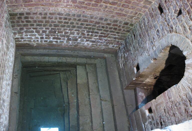 Photo of a rectangular stone and brick pool partially filled with water, with a stairway descending into it and an arched door.