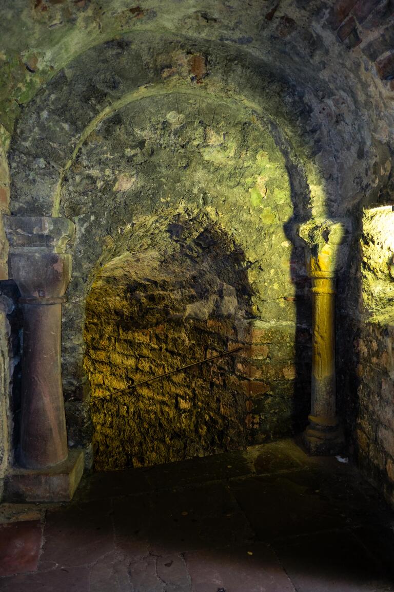 Photo of a stone archway framed by columns and leading to a descending passageway made of rough stone.