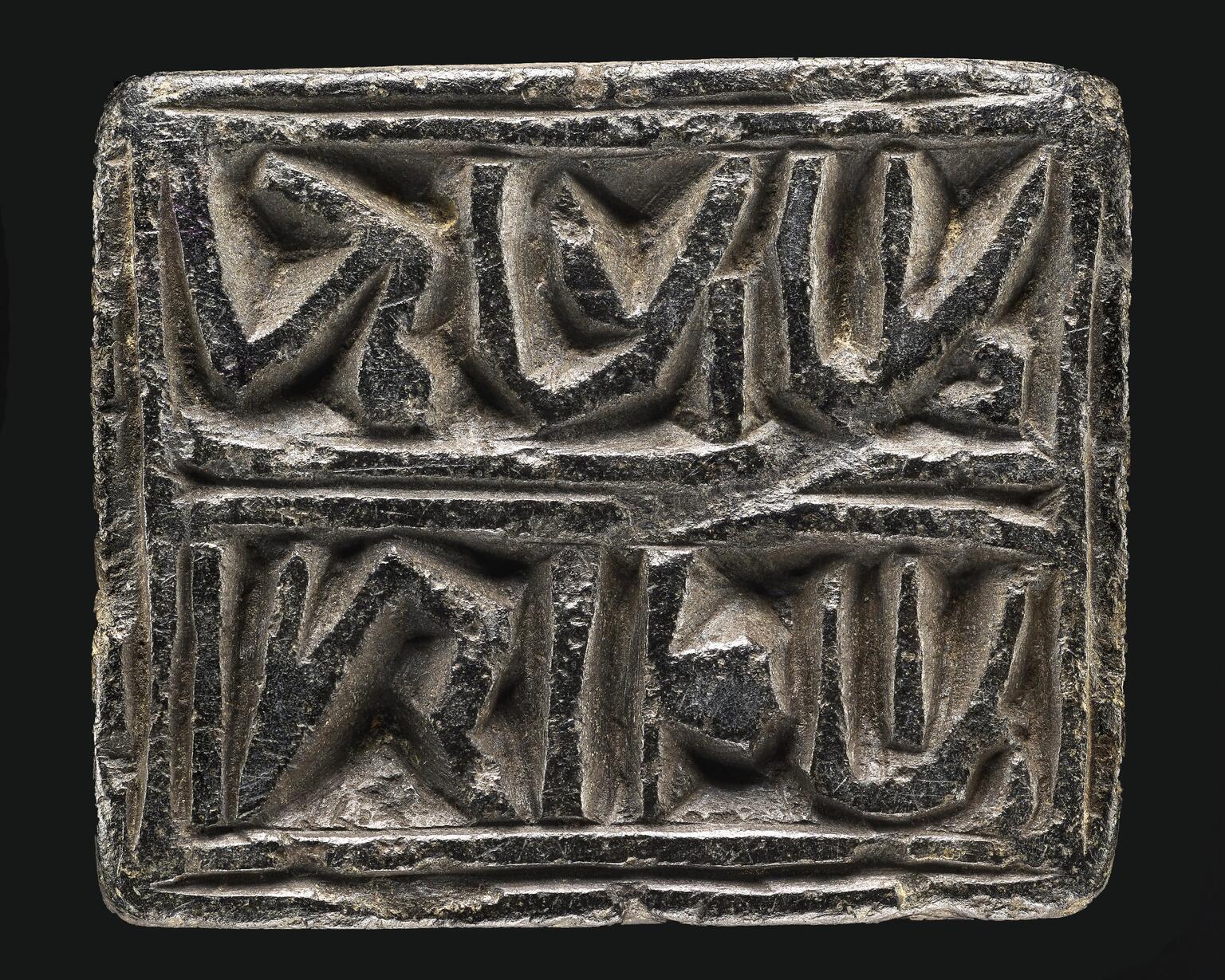 Photo of a rectangular black stone block inscribed with two outlined words of reversed Hebrew writing.