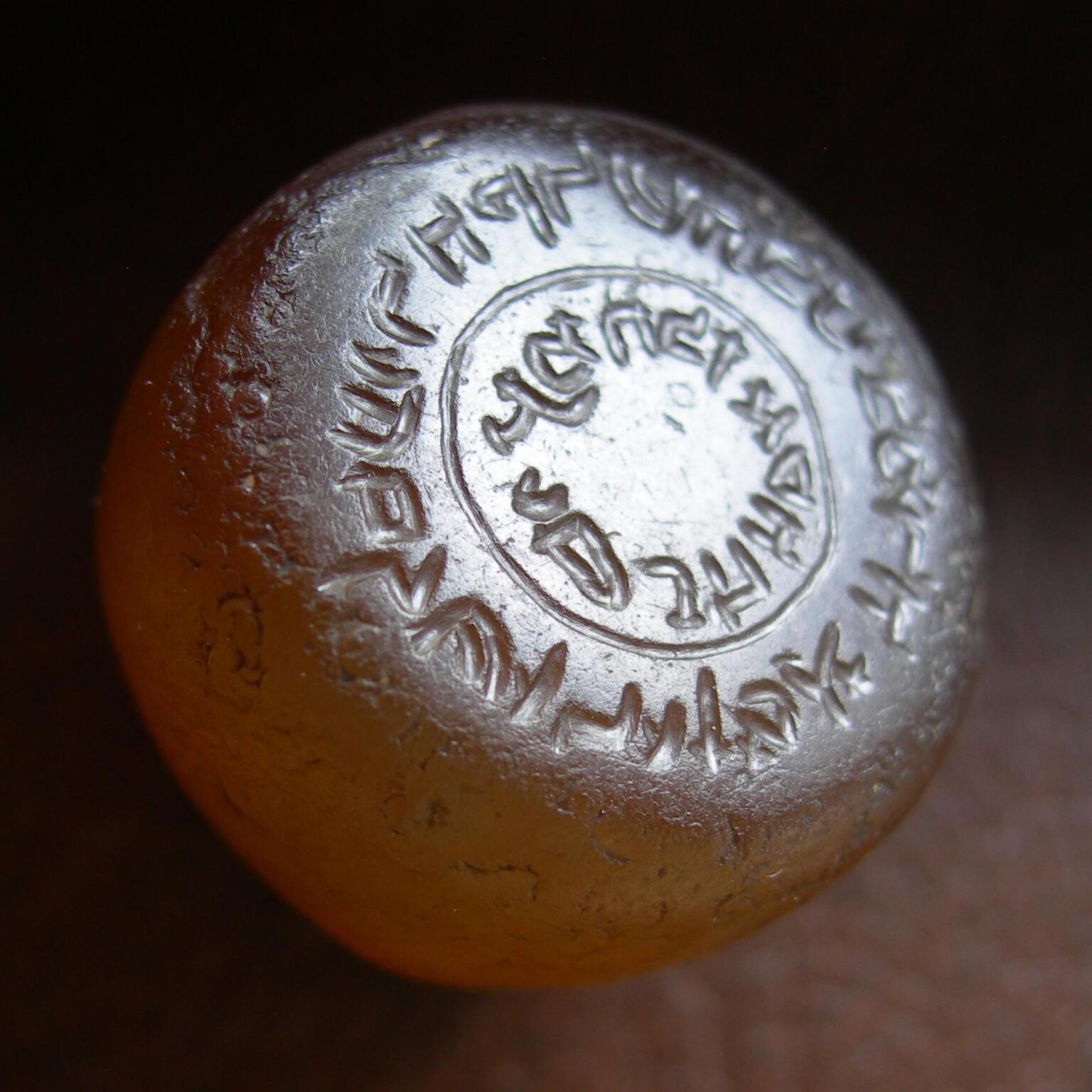 Photo of a rounded orange object inscribed with reversed Hebrew writing in concentric circles, viewed at an angle.