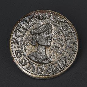 Round bronze seal with a turbaned bust in profile and floral decoration, encircled by reversed Hebrew text.