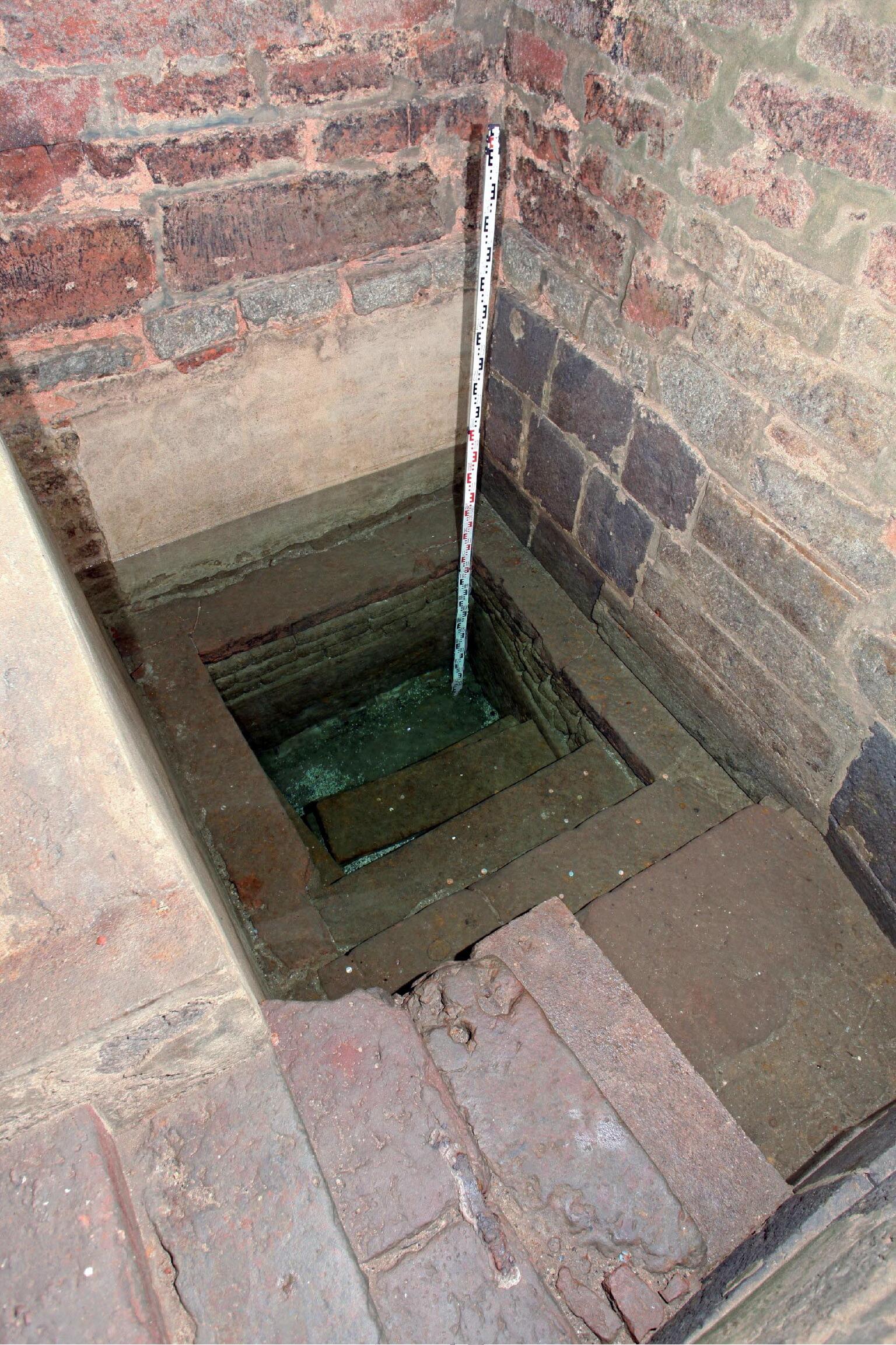 Photo of a square stone-and-brick-lined pool, with steps leading down.