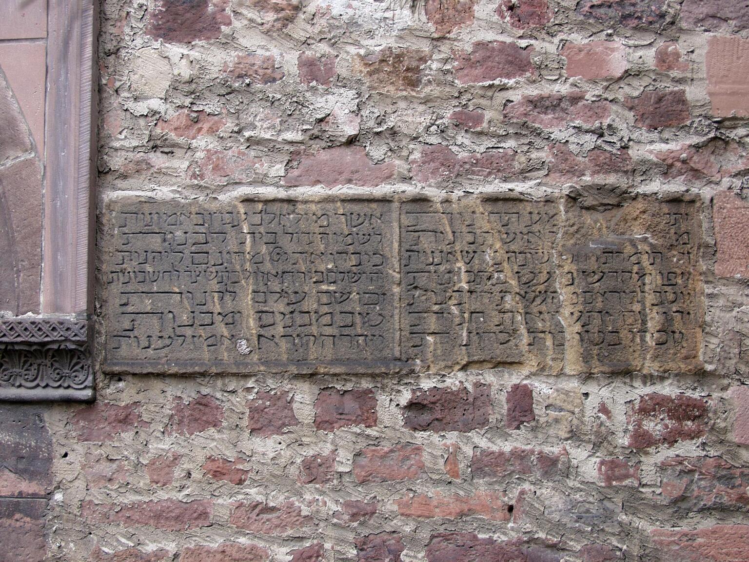 Photo of a weathered stone plaque with Hebrew inscriptions set into a rough brick wall.