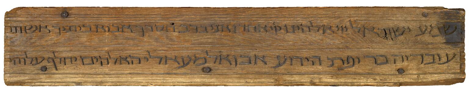 Rectangular mounted wooden plaque with two lines of carved Hebrew script.