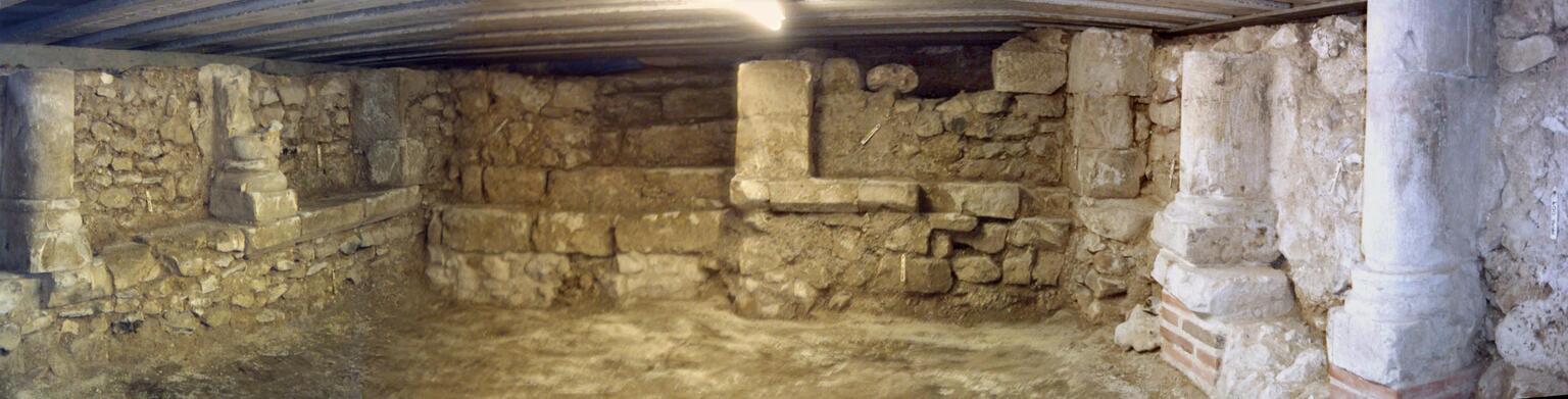 Photo of the bottom part of a stone and brick room with rough, uneven walls and partial columns.