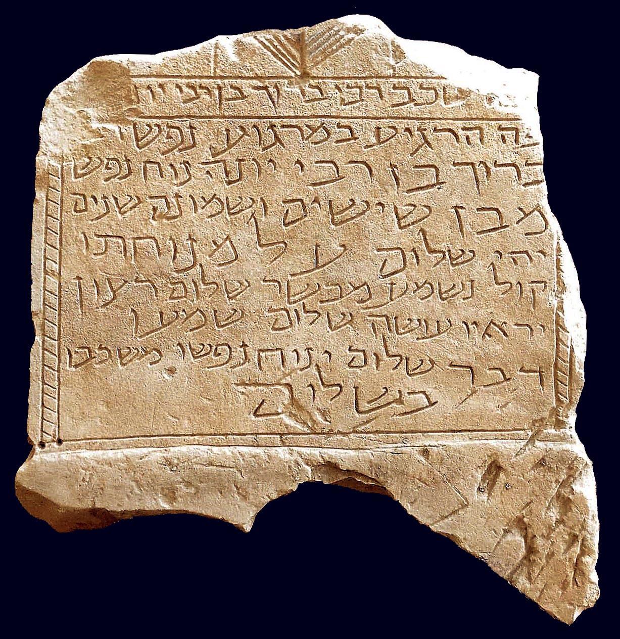 Photo of a broken, jagged stone slab with a Hebrew inscription, including a separated heading, decorative borders, and a simple candelabrum.