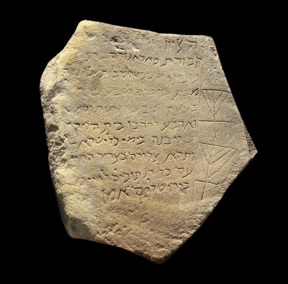 Hexagonal, weathered stone tablet inscribed with Hebrew text and two simple ritual candelabrums.