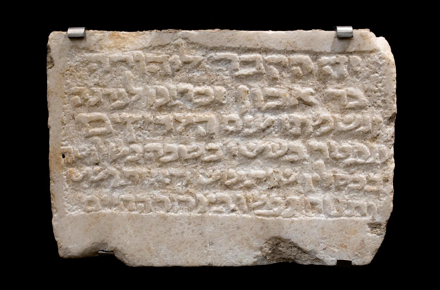 Rectangular white stone tablet with six lines of Hebrew relief text.