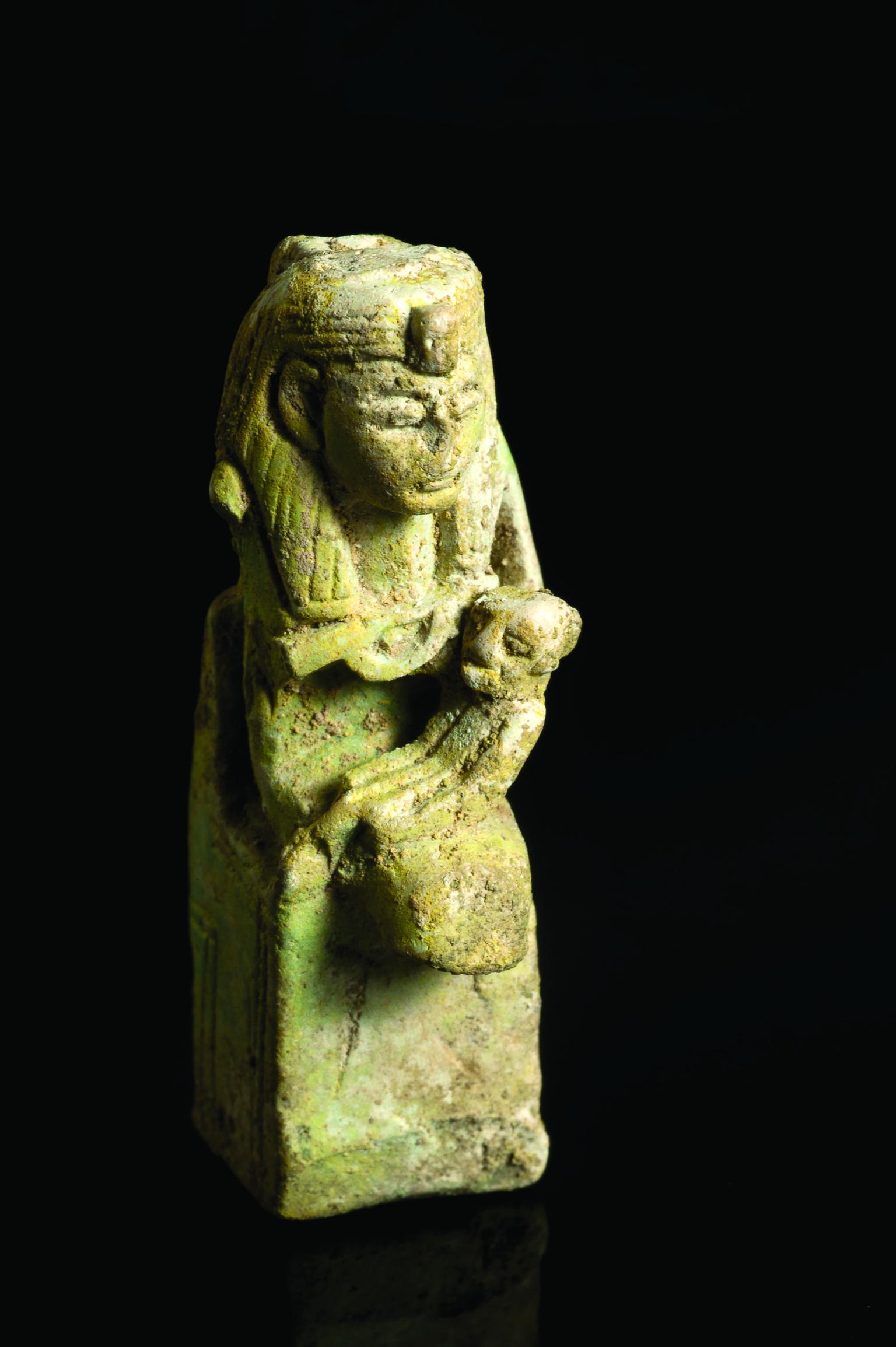 Faience amulet with Egyptian goddess wearing headdress sitting on a throne and holding a child.